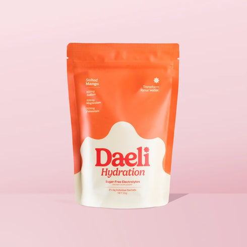 A stand-up pouch of Daeli Hydration Salted Mango sugar-free electrolyte powder, featuring a bright orange top and bottom with a white central splash shape and red brand lettering, set against a solid light pink background.