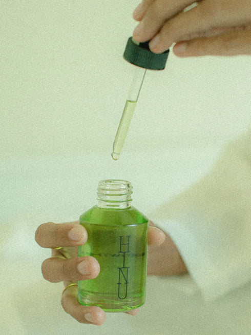 Hand holding a green dropper bottle with a dropper on a light background
