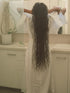 Person with long hair standing in a bathroom, wearing a white robe.