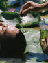 Person lying on water lilies with another hand holding a bottle of green liquid.