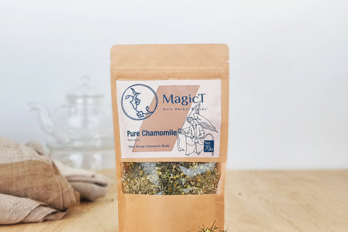 Bag of MagicT Pure Chamomile on a wooden surface with chamomile flowers spilling out.
