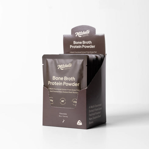 Mitchell's Bone Broth Protein Powder in a chocolate flavor, shown in a retail display box with individual pouches visible inside, on a clean white background.