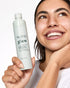 Woman holding a Natio Glow skincare product with a plain background