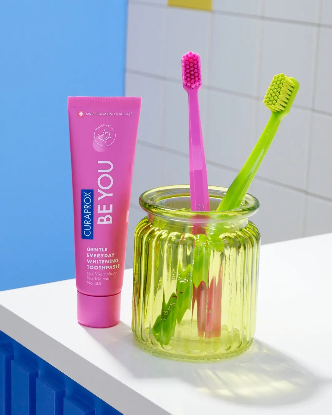 Curaprox Be you Watermelon tube and toothbrushes on a bathroom shelf