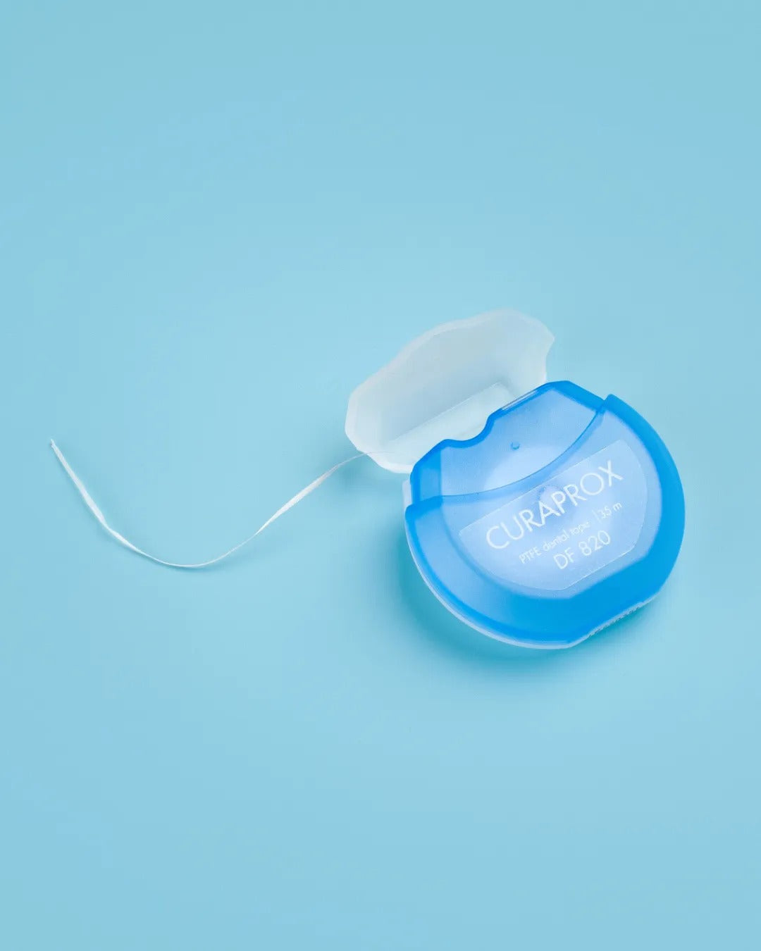 Curaprox DF 820 dental tape dispenser on a blue background