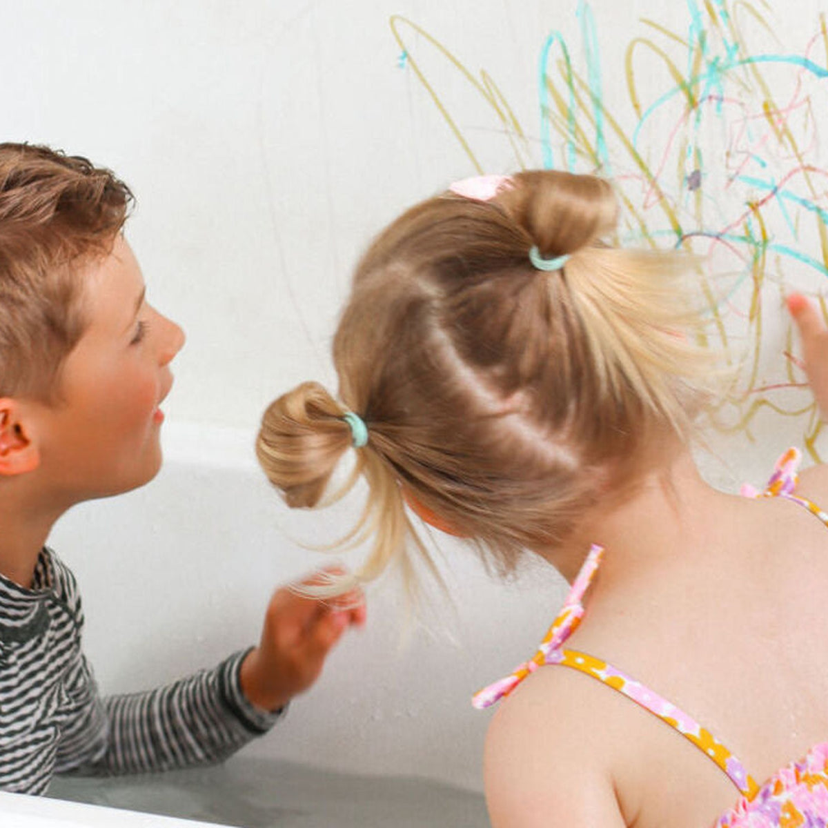 Two children drawing on the bathroom wall with the bath crayons