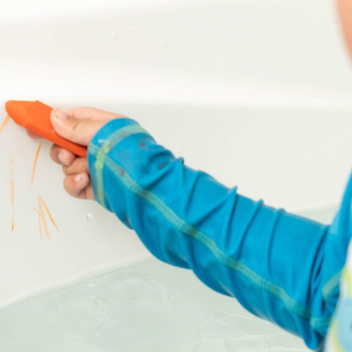 A child drawing on a wet bath surface with an orange bath crayon