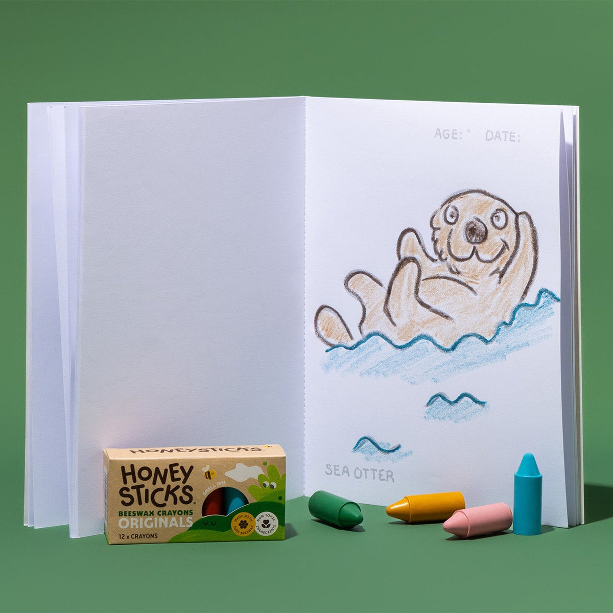 The book open at a sea otter page with Honeysticks crayons alongside