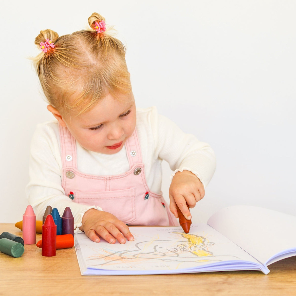 A toddler colouring a page of the book with a crayon