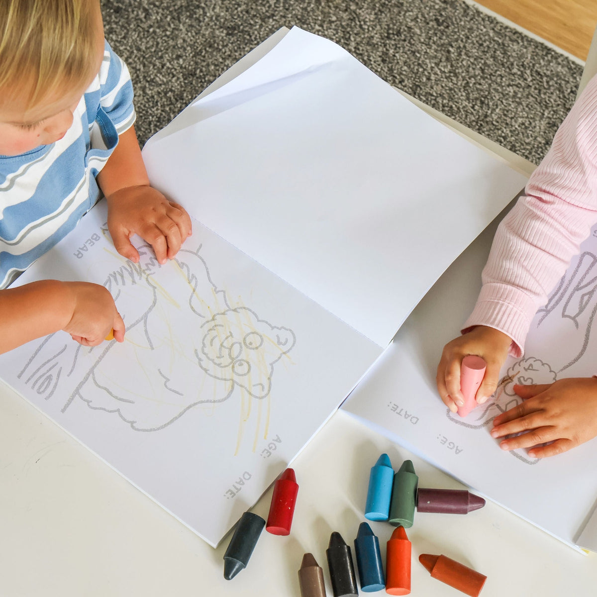 Two children colouring pages from the book on the floor