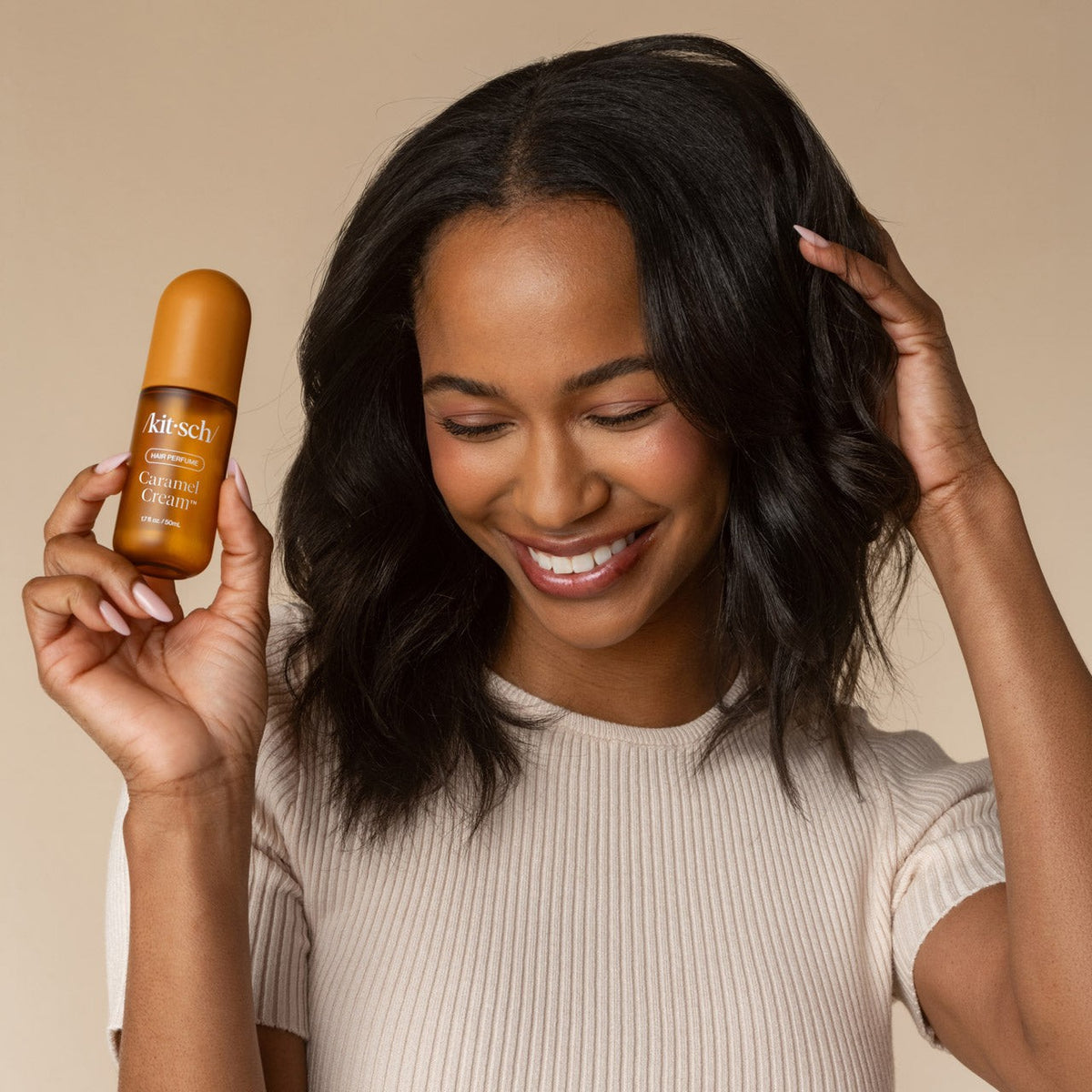 Woman holding the Kitsch Caramel Cream mist beside her hair
