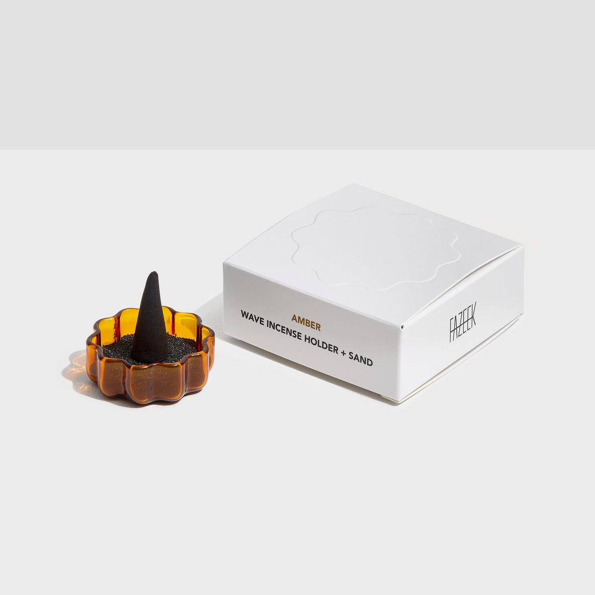 Fazeek amber Wave incense holder with a cone burning in it, shown beside its box