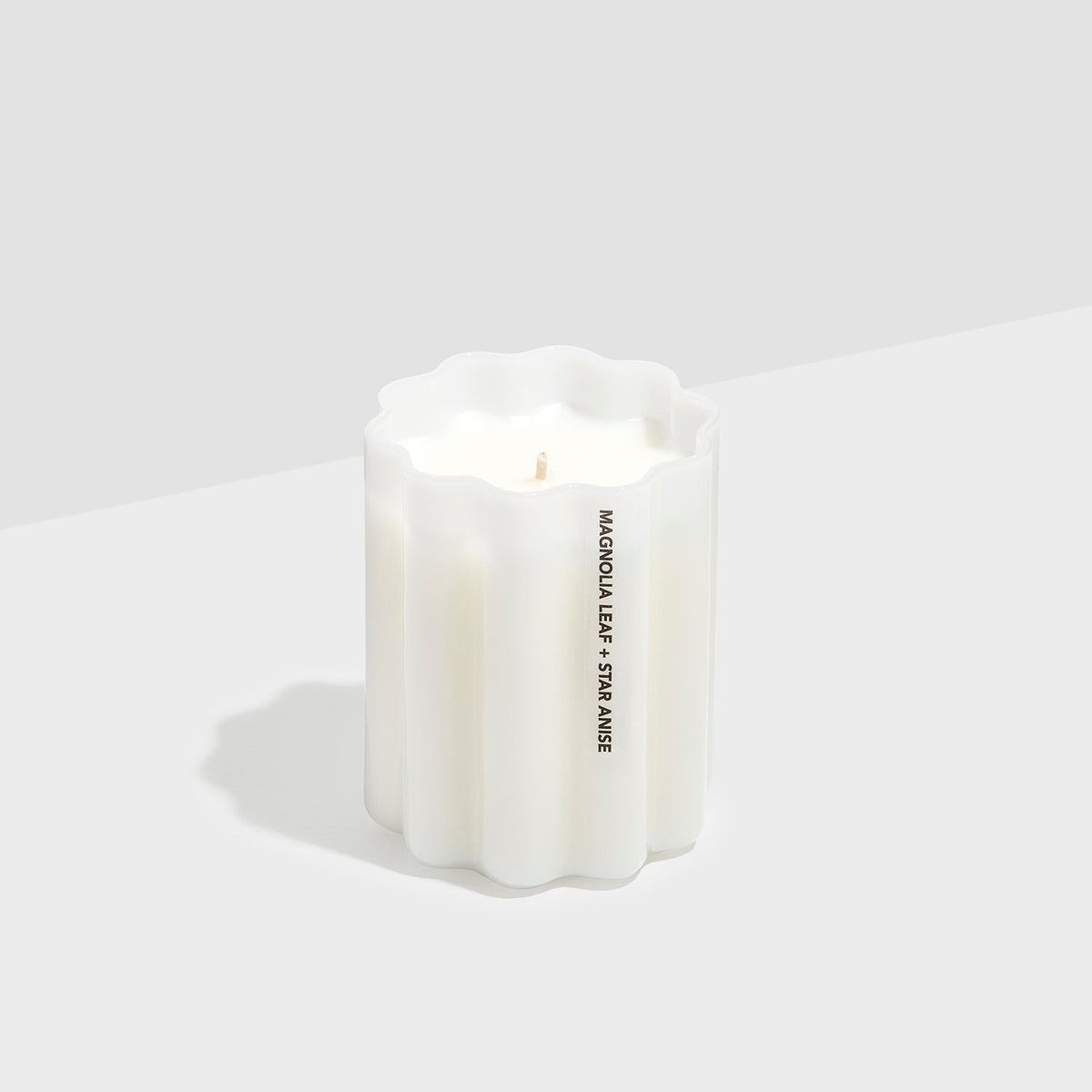 Fazeek Wave Candle in rippled white glass, lit, showing the wave shape