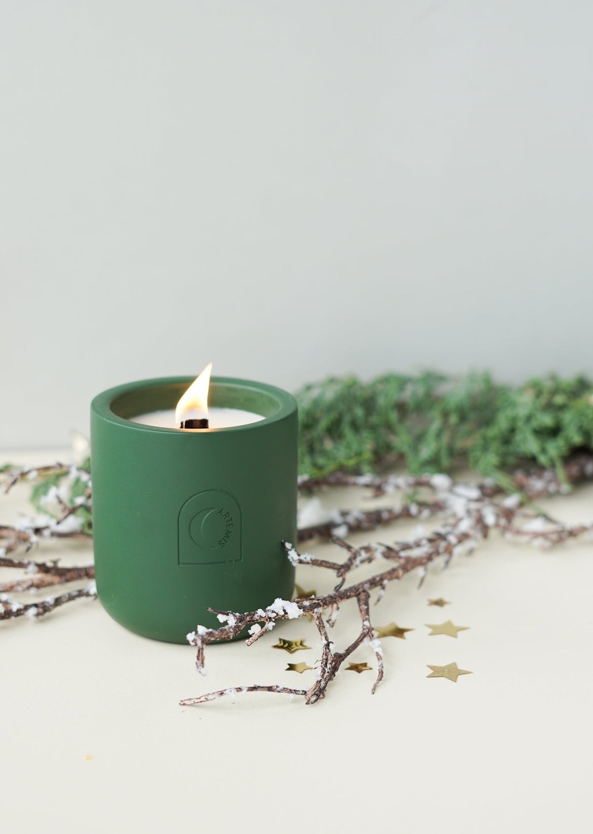The Under The Mistletoe candle lit, surrounded by winter greenery