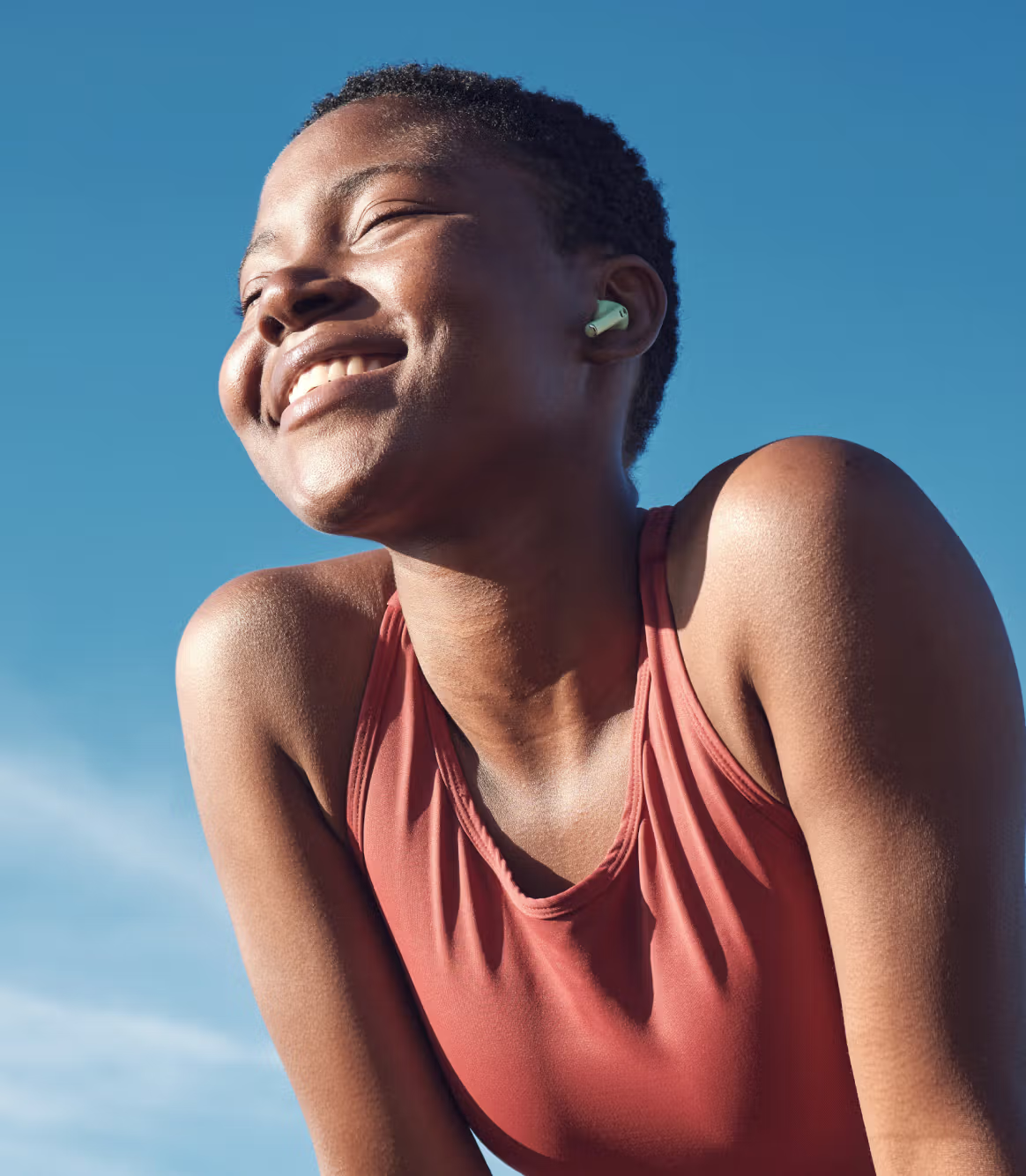 Woman wearing wireless earbuds against a clear blue sky