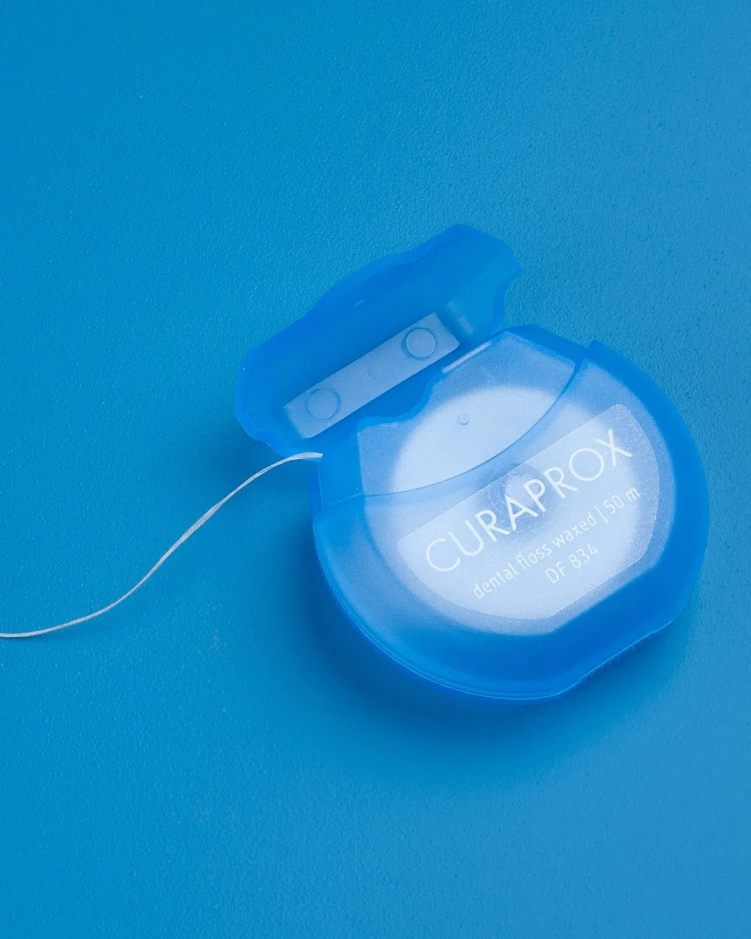Curaprox DF 834 dental floss dispenser on a blue background