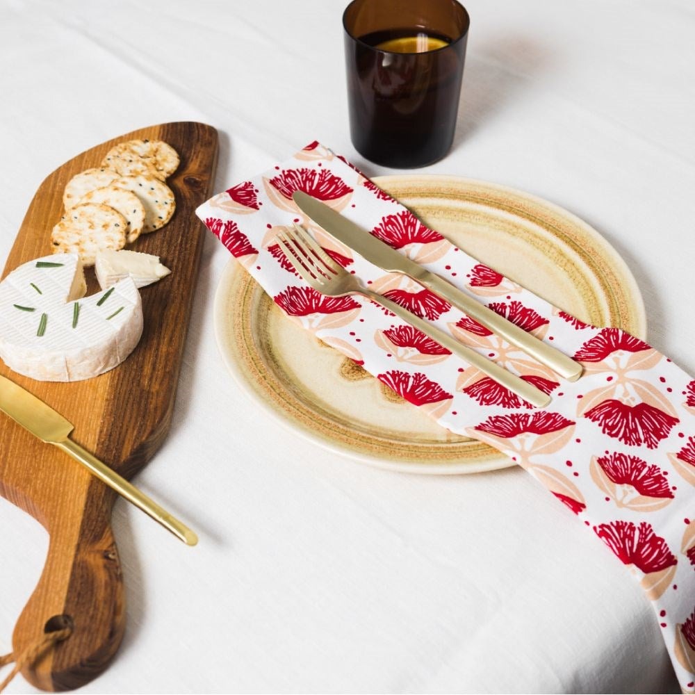 The pohutukawa napkins in red on a set table with a wooden board