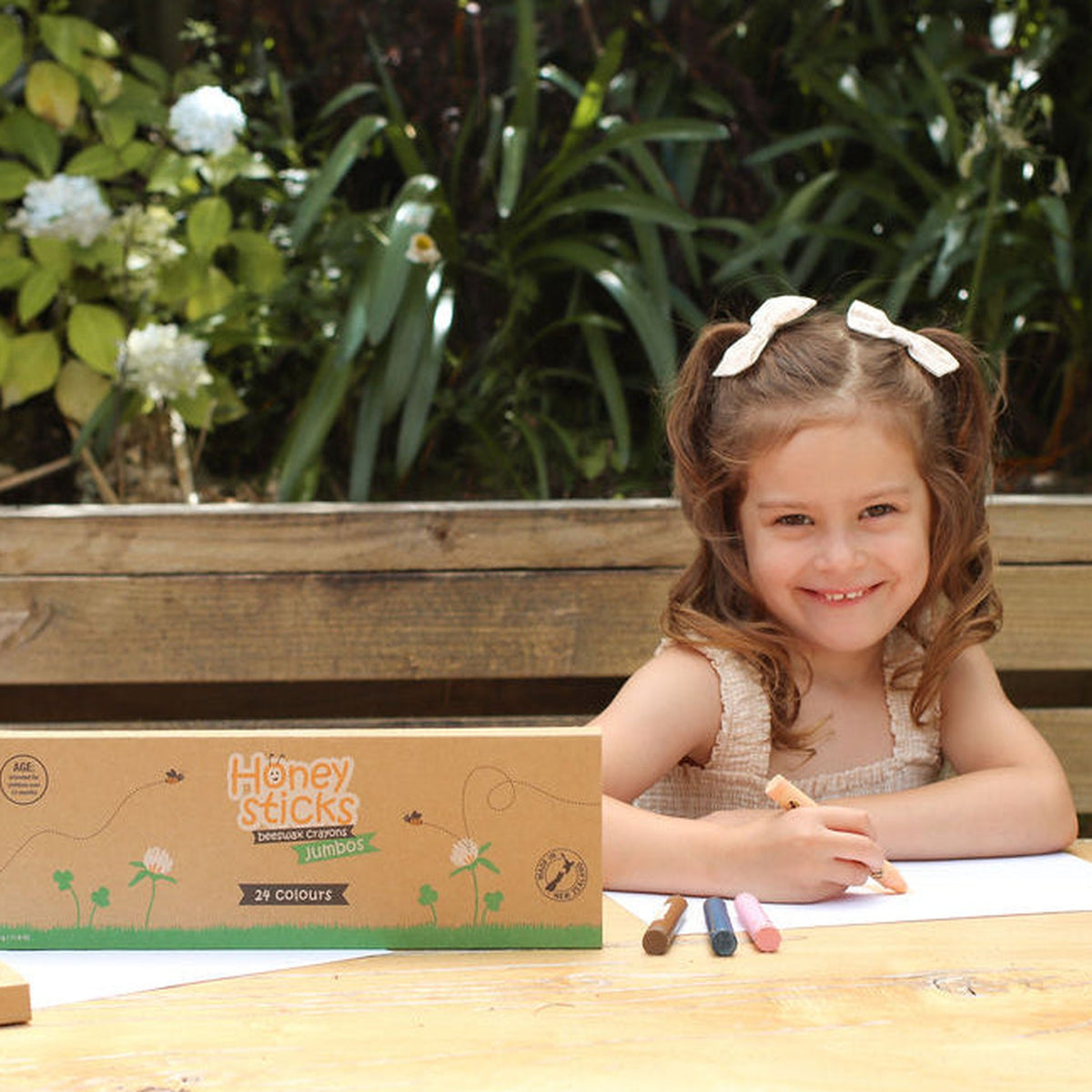 A child drawing at an outdoor table with the Jumbo 24 Pack open beside her
