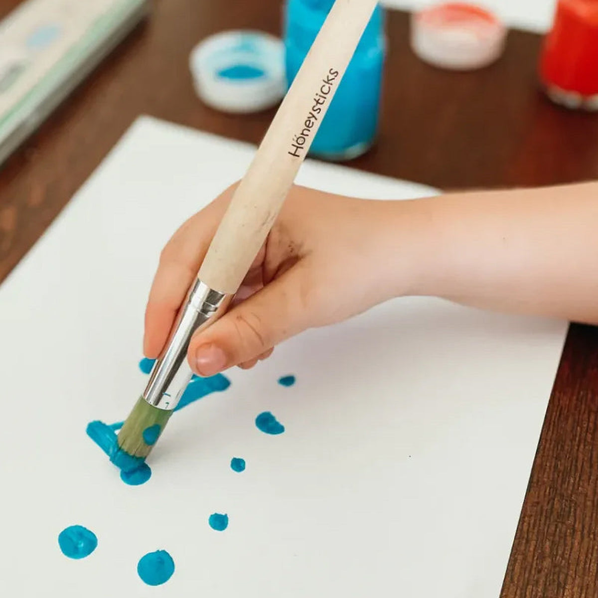 A child painting blue dots on paper with a jumbo brush