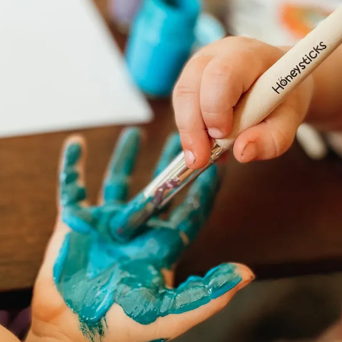 A child painting their own hand with a jumbo brush