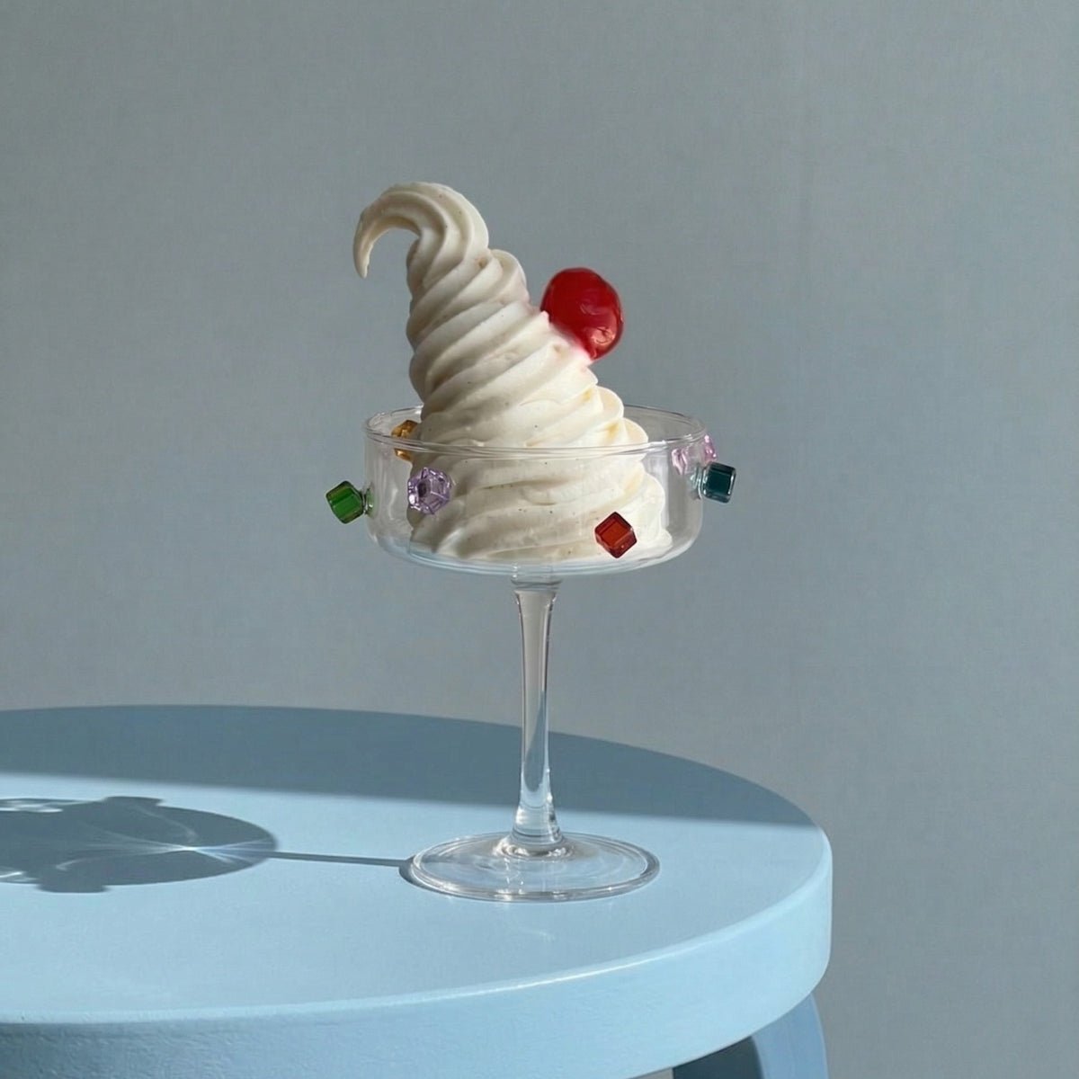 A Fazeek Jewel Coupe holding soft serve with a cherry, on a blue table