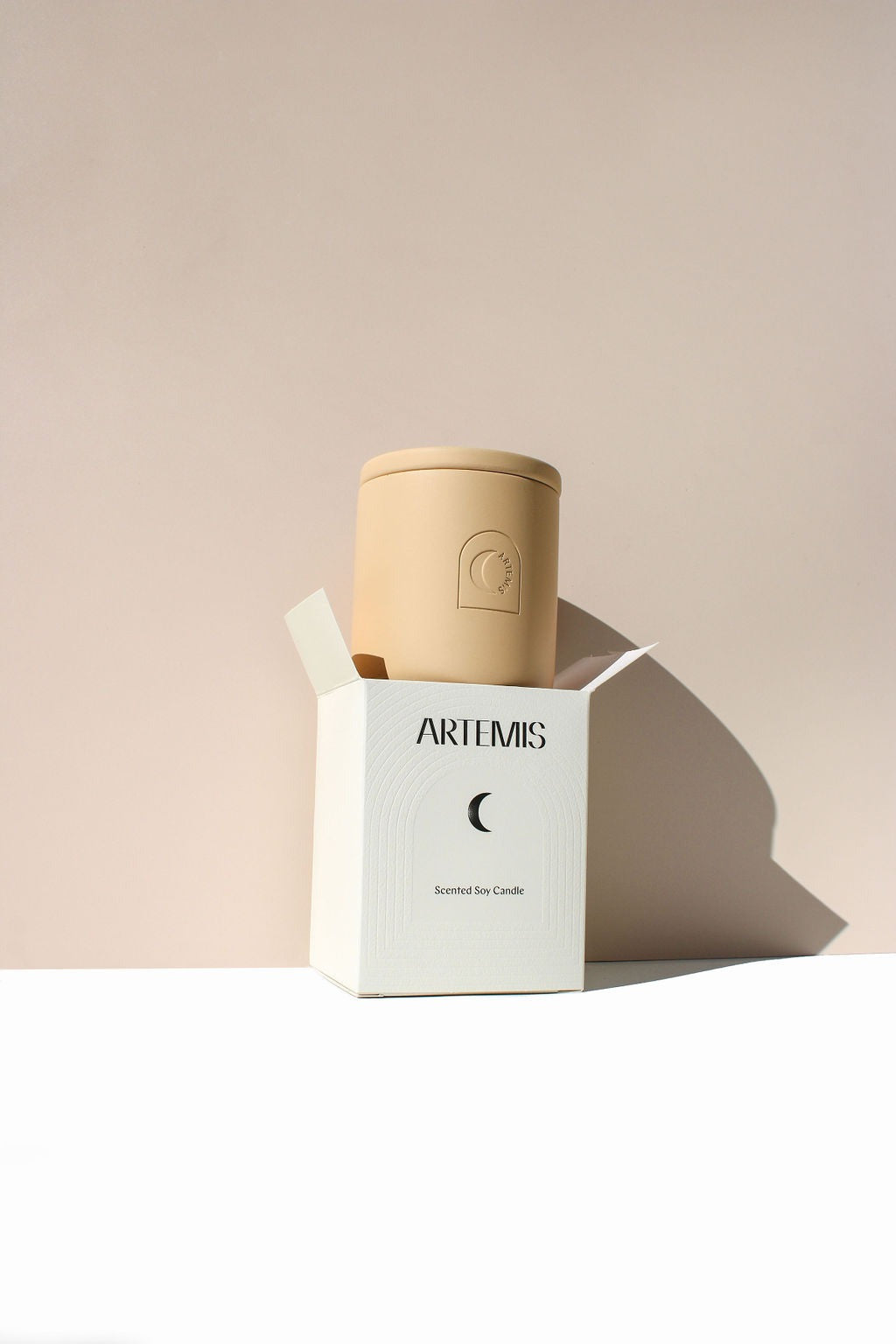 Artemis Aster soy candle in a sand-coloured vessel beside its box