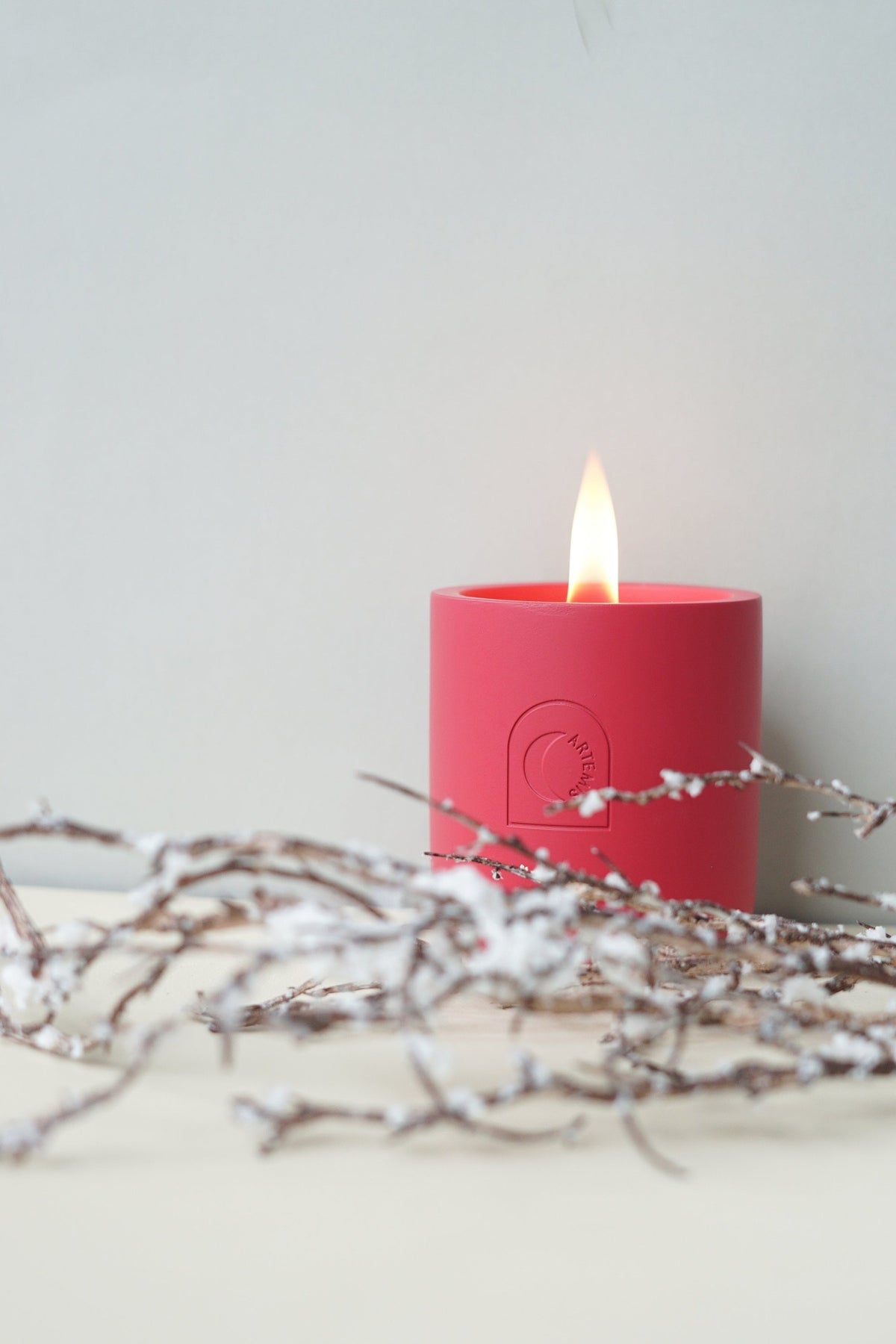 The Festive Delight candle burning, styled with frosted branches