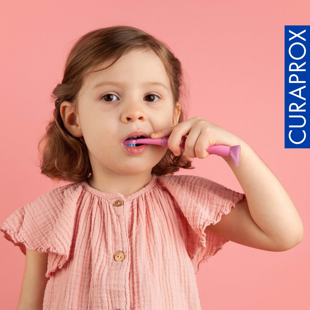 A young child holding a Curaprox baby toothbrush