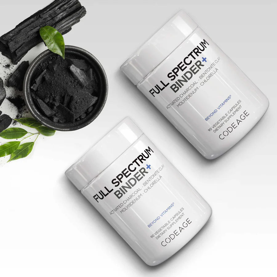 Two bottles of Codeage Full Spectrum Binder+ beside a dish of activated charcoal and green leaves