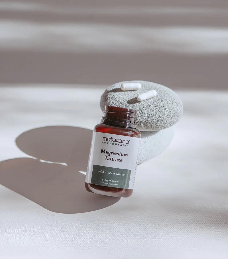 Bottle of matakana magnesium taurate with a stone and pills on a neutral background