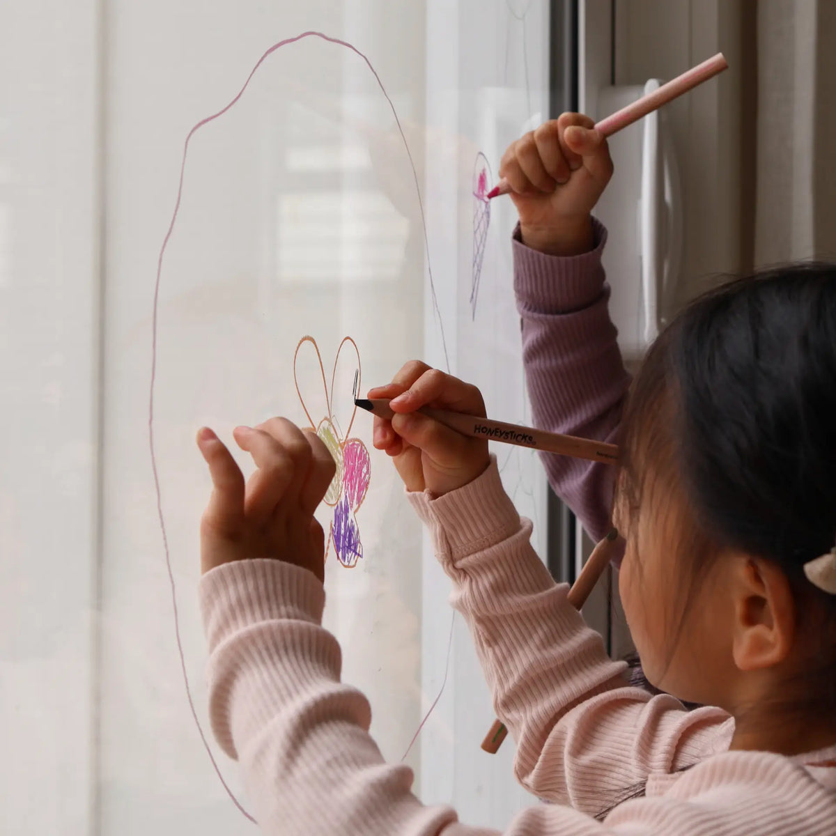 A child drawing on a window with a jumbo triangle pencil