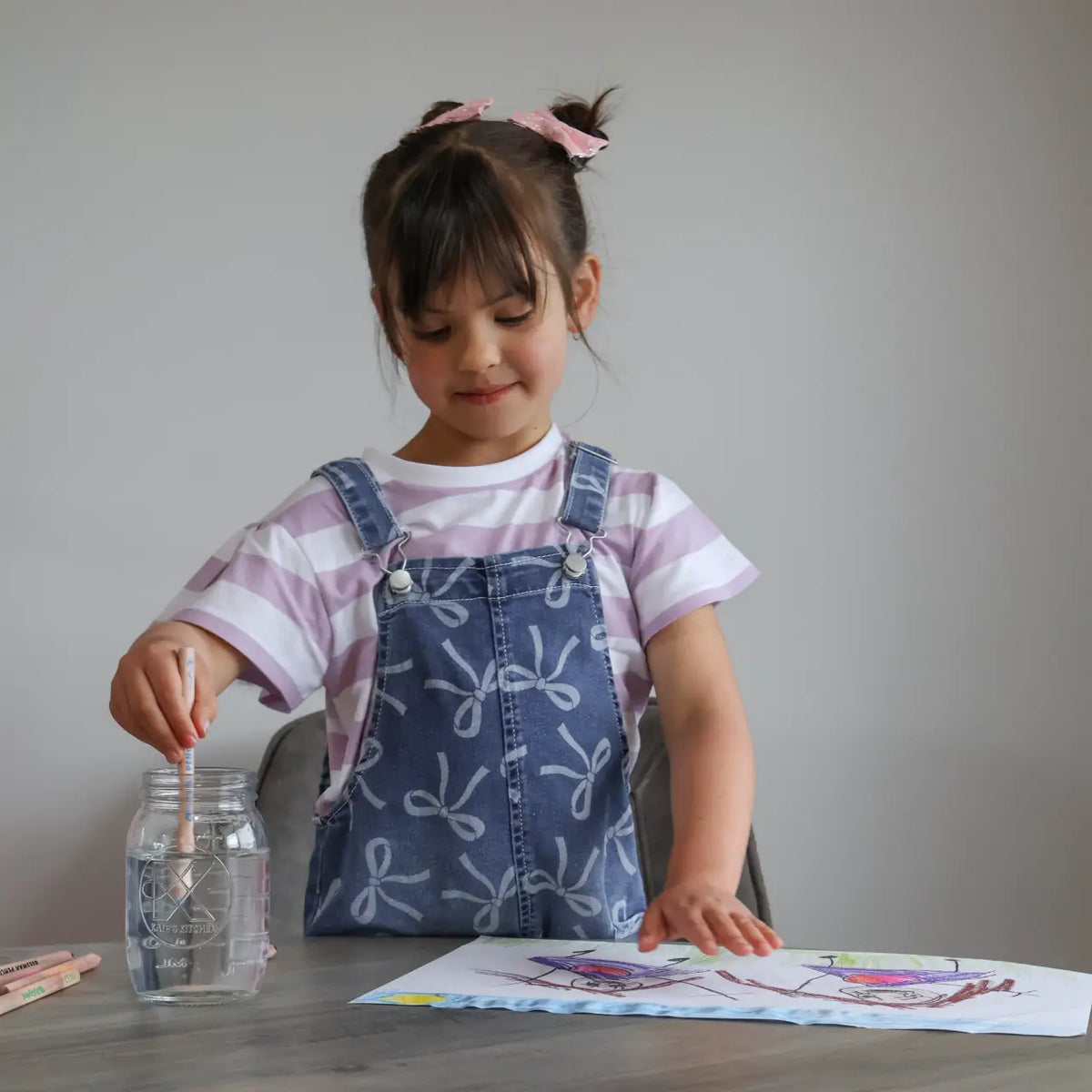 A child drawing at a table with a glass of water beside the paper