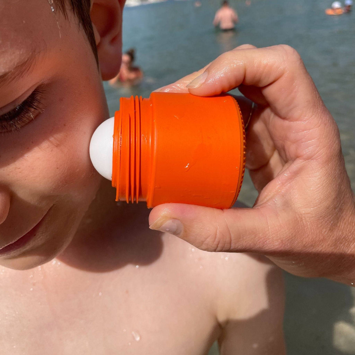 A Solmates applicator being rolled onto a child's face at the beach