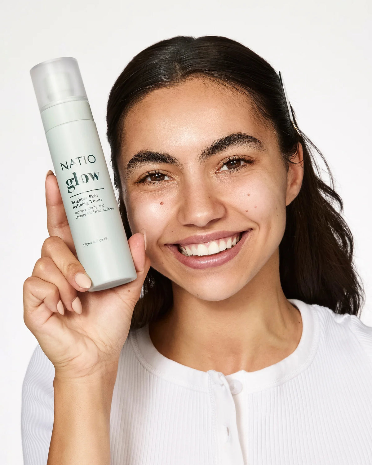Woman holding a bottle of Natio Glow product against a white background