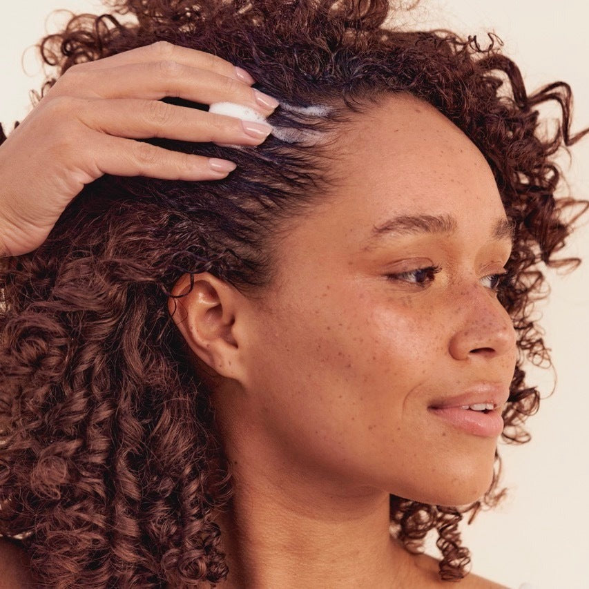 Woman with curly hair massaging Hair Gain Scalp Foam into her scalp