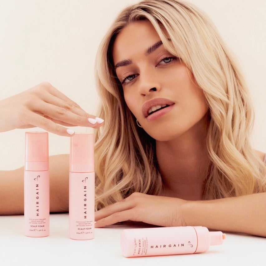 Woman resting her hands beside three Hair Gain Scalp Foam bottles