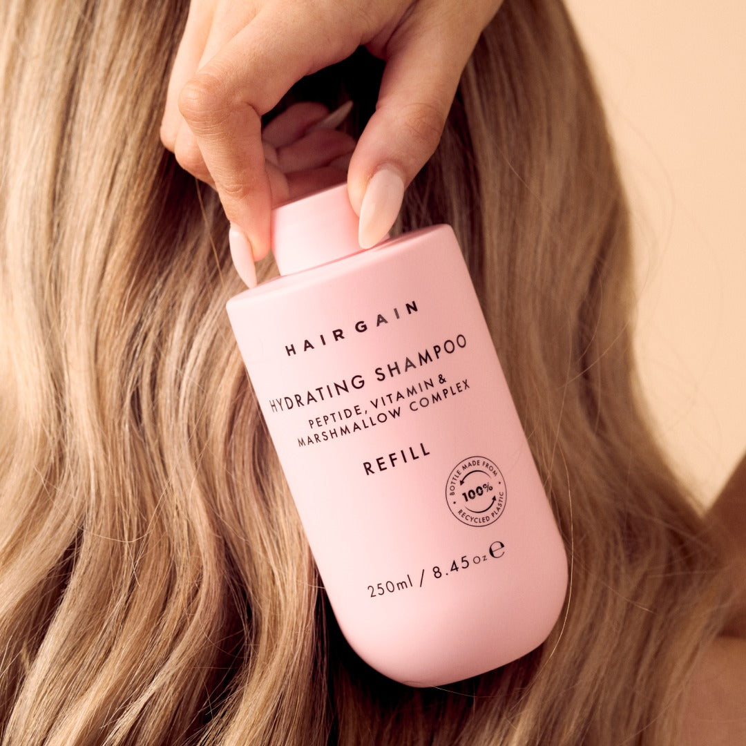 Hand holding the Hair Gain Hydrating Shampoo refill against long hair