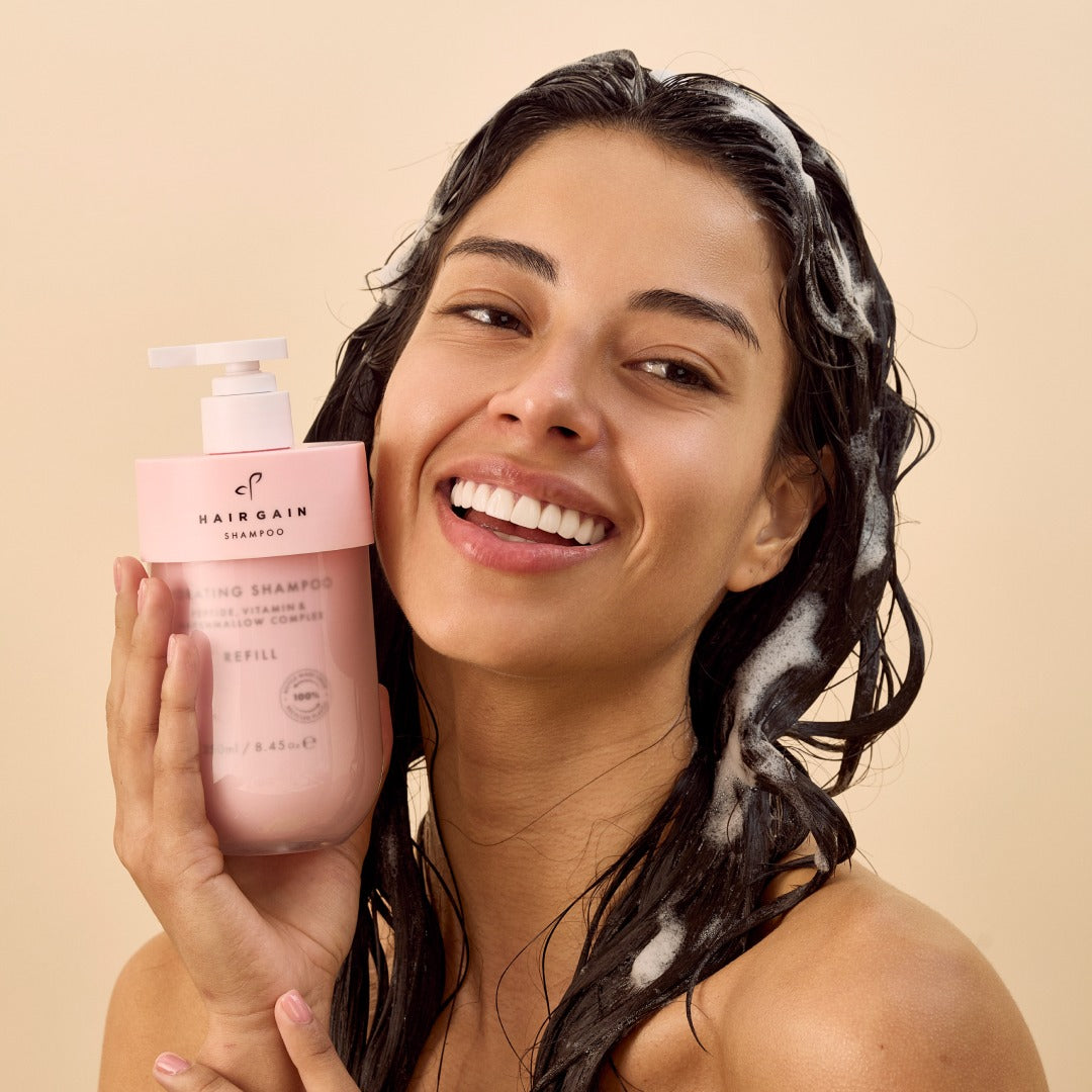 Woman with lathered hair holding the Hair Gain shampoo pump bottle