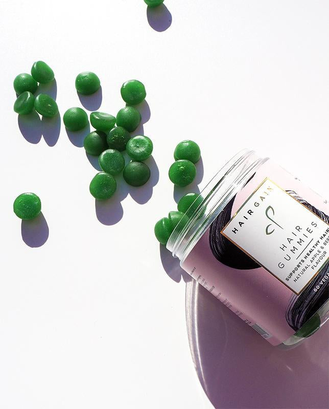 Hair Gain Hair Gummies jar tipped over with green gummies spilling out
