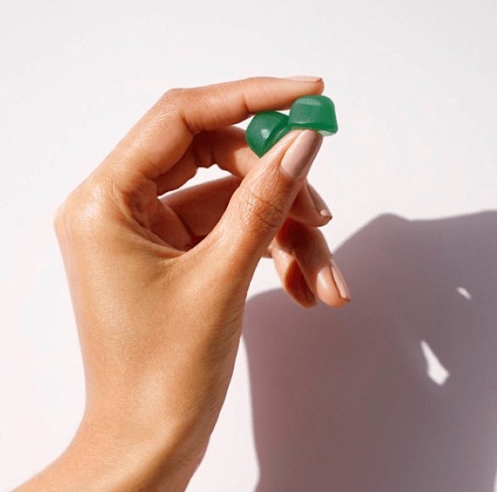 Fingers holding a single green Hair Gain gummy