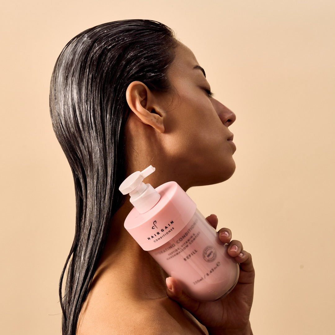 Woman with wet hair holding the Hair Gain Hydrating Conditioner pump bottle