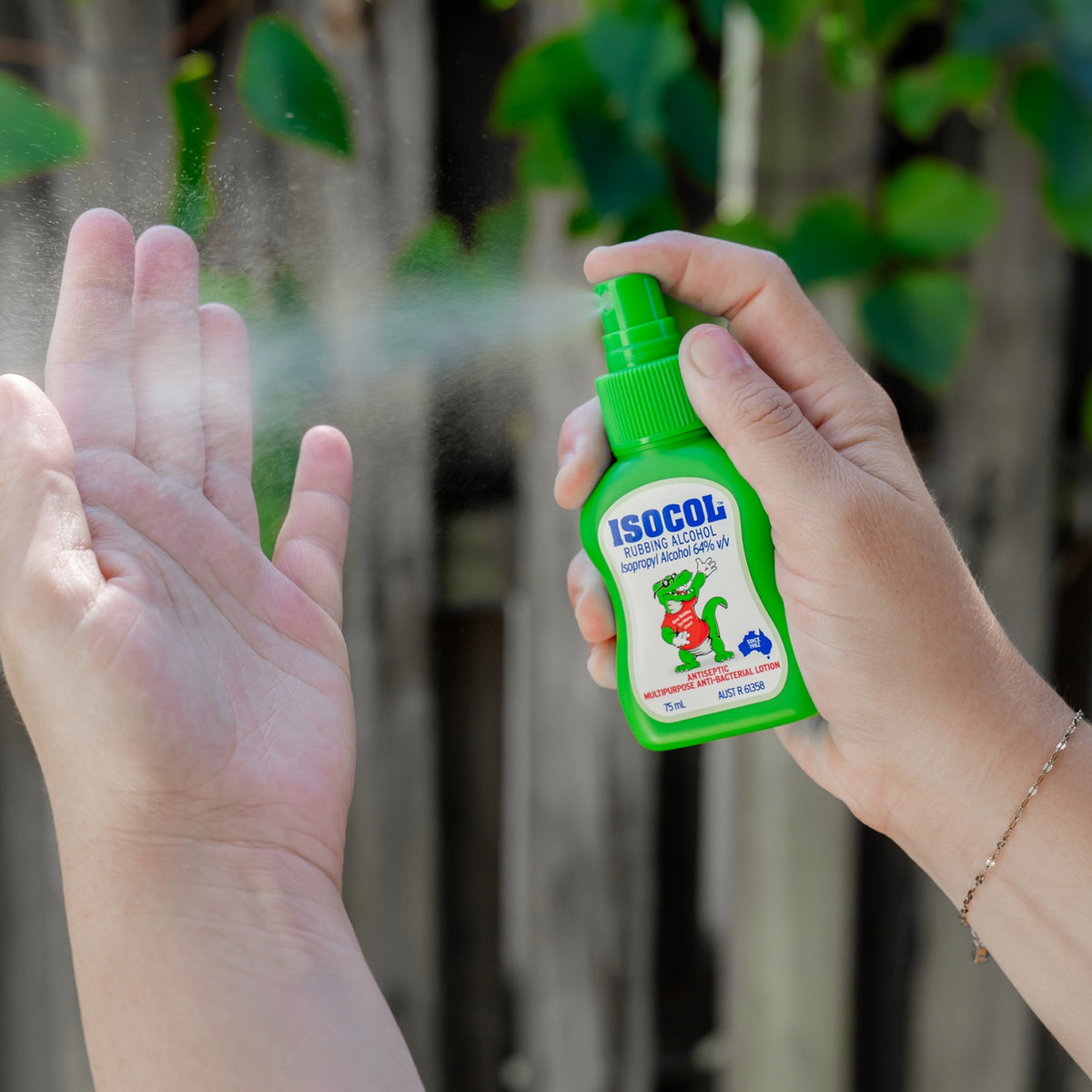 Hands spraying Isocol Rubbing Alcohol onto an open palm outdoors