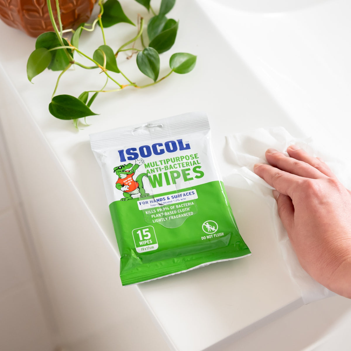 A hand wiping a white bathroom benchtop beside the Isocol anti-bacterial wipes pack