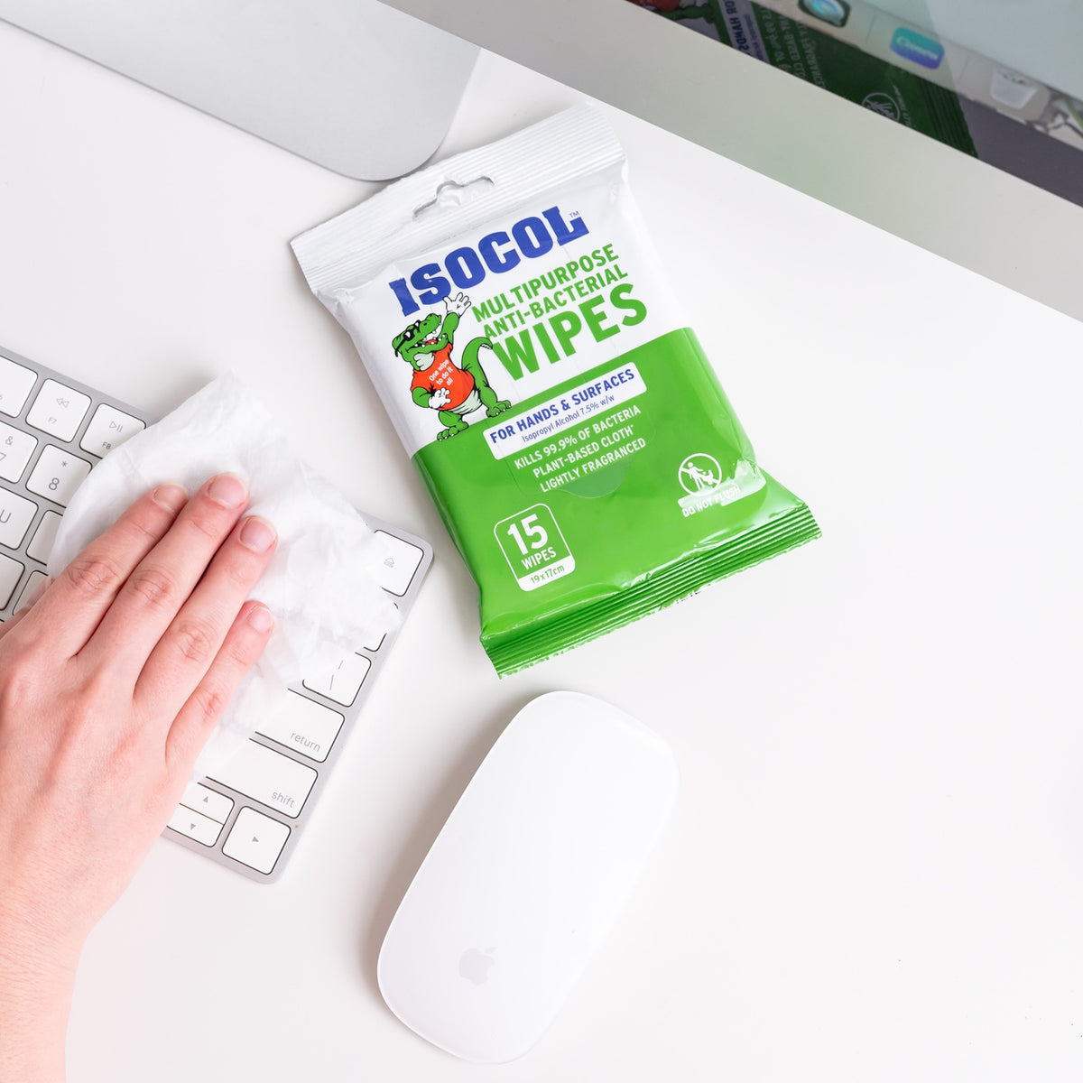 A hand wiping a white keyboard with an Isocol wipe, pack and mouse on the desk