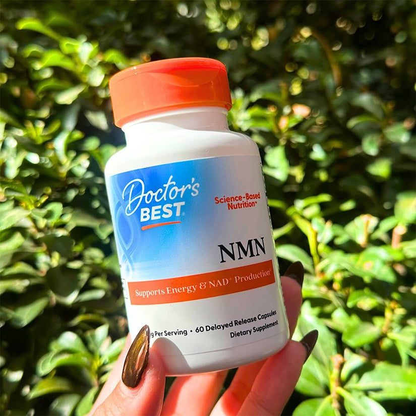 Doctor's Best NMN 60 capsule bottle held in hand outdoors in front of green leaves
