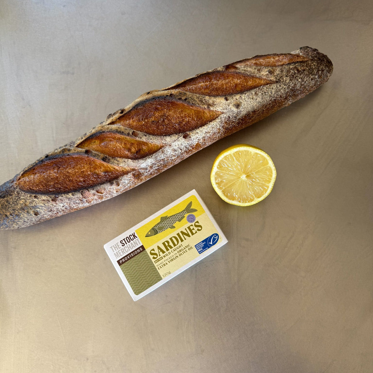 Open tin of sardines beside a sliced baguette and a lemon half