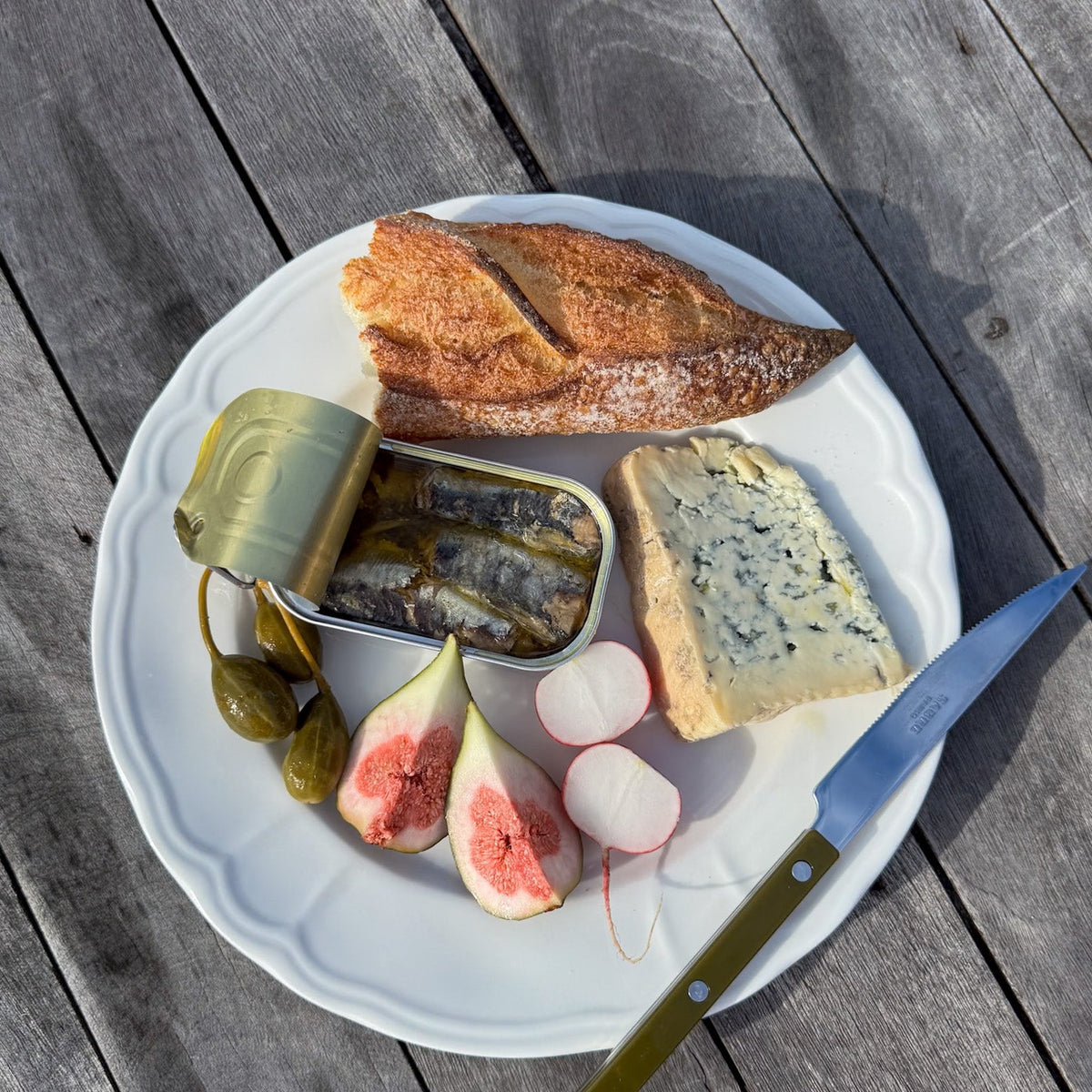 Open tin of sardines on a plate with figs, radish and cheese
