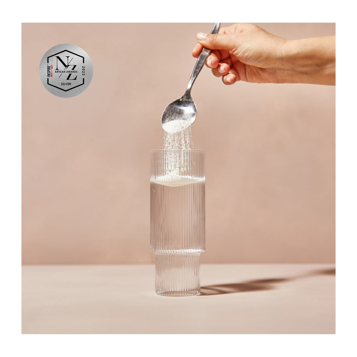 A scoop of Soochi collagen powder being stirred into a glass of water