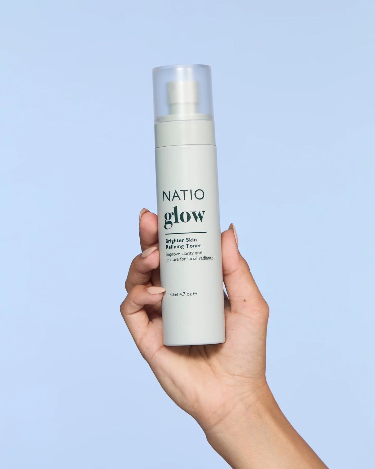 Hand holding a Natio Glow skincare product against a light blue background