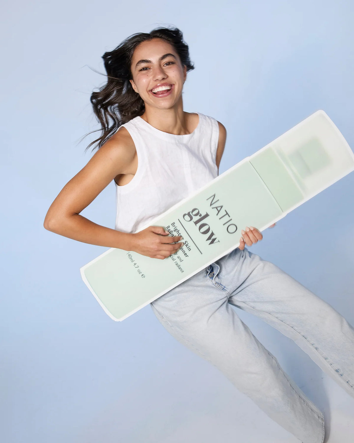 Woman holding a large box of Natio Glow against a light blue background